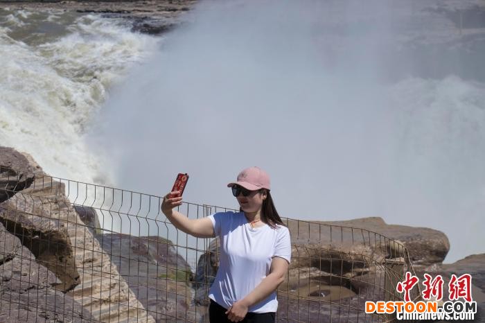 图为游客在瀑布前拍照留念。 杨峰 摄